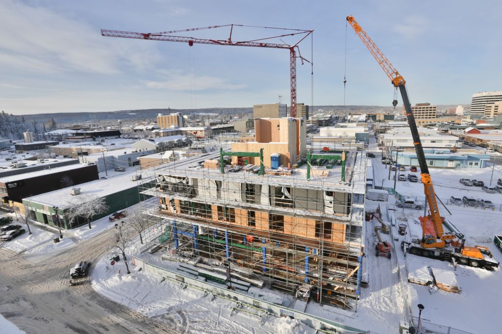 Aerial views of the worksite show the cross-laminated timber (CLT) core, the glued-laminated (glulam) columns and beams, and the structural insulated panels (SIPs) of the envelope.