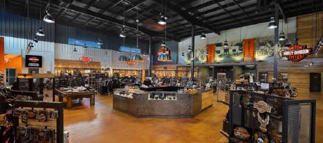 The showroom features high ceilings with a mix of hard and soft design elements. Steel is tempered by warm colors, including the signature Harley-Davidson orange. The walls also incorporate wood planks.