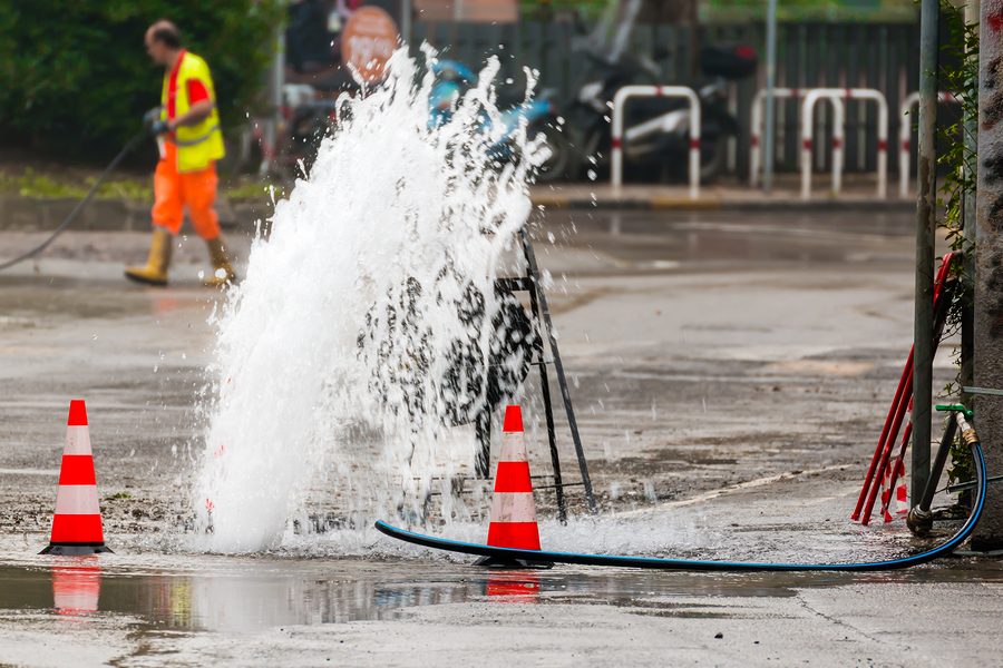 Road Spurt Water Beside Traffic Cones And A Technician In Backgr