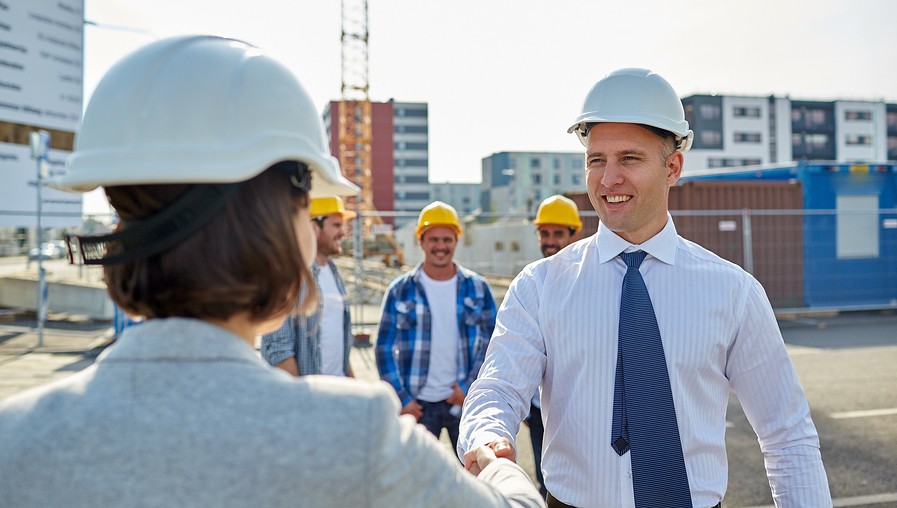 business, building, teamwork, gesture and people concept - group of smiling builders or architects in hardhats greeting each other by handshake on construction site