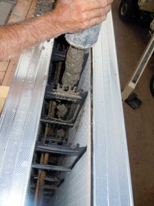 Concrete being pumped into the top of the wall. The steel reinforcement, held in position by the ICF webs, is visible.