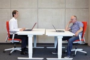 The man on the right is showing correct posture when working at a desk, while the man on the left is showing poor posture. Photo c bigstock.com