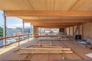 Construction photo showing cross-laminated timber (CLT) floor, glulam beams, and slender steel column supports on west side of the building.