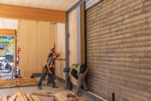 Installation of the Passive House compliant zero lot line party wall, with prefabricated cross-laminated timber (CLT) panels that were lowered into the slot by crane and the vapour barrier was sealed from the interior.