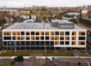 An aerial view of the residential project, showing the compact low-rise form and the rooftop solar panel installation.