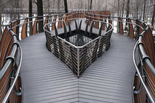 A cable railing system running down the sides of and bordering an opening on a pedestrian bridge.