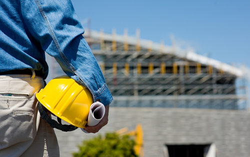 close up shot of a construction worker with his hat in his hand and looking at a construction site