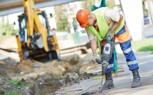 Builder worker with pneumatic hammer drill equipment breaking asphalt at road construction site