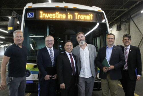 four men of differing heights standing in front of a transit bus