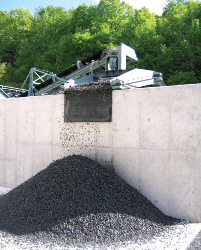 A conveyor system deposits crushed aggregate onto a storage pile against a concrete wall.