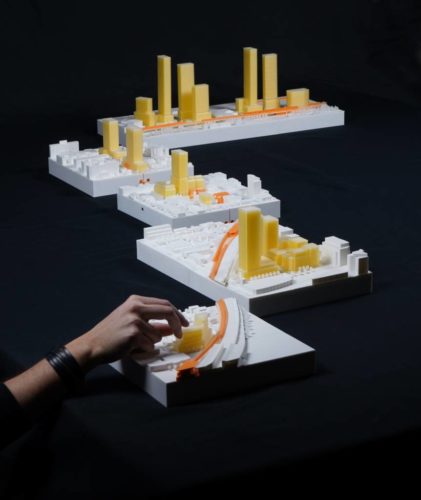 A conceptual architectural model at DesignTO Festival, featuring white and yellow city structures with interactive design elements.