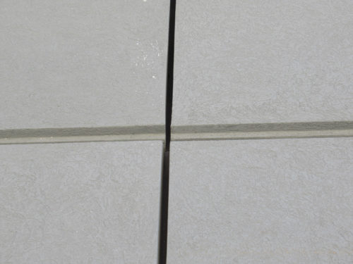 A close-up view of gray floor tiles showing a noticeable crack running between two tiles. The tiles have a smooth texture and are arranged in a grid pattern.