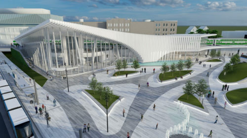 Bird's-eye view of a modern transit hub with a striking curved glass facade and white vertical fins. The plaza features a mix of pathways, green spaces, trees, and a fountain, with people walking and gathering.