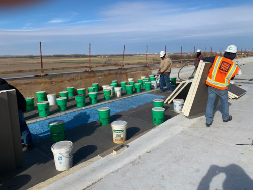 Construction workers are on a roof, arranging buckets and materials for a project.