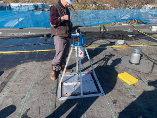 Worker on a rooftop adjusting equipment; safety tools and materials are visible.