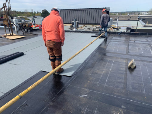 Two workers install roofing material on a flat rooftop.