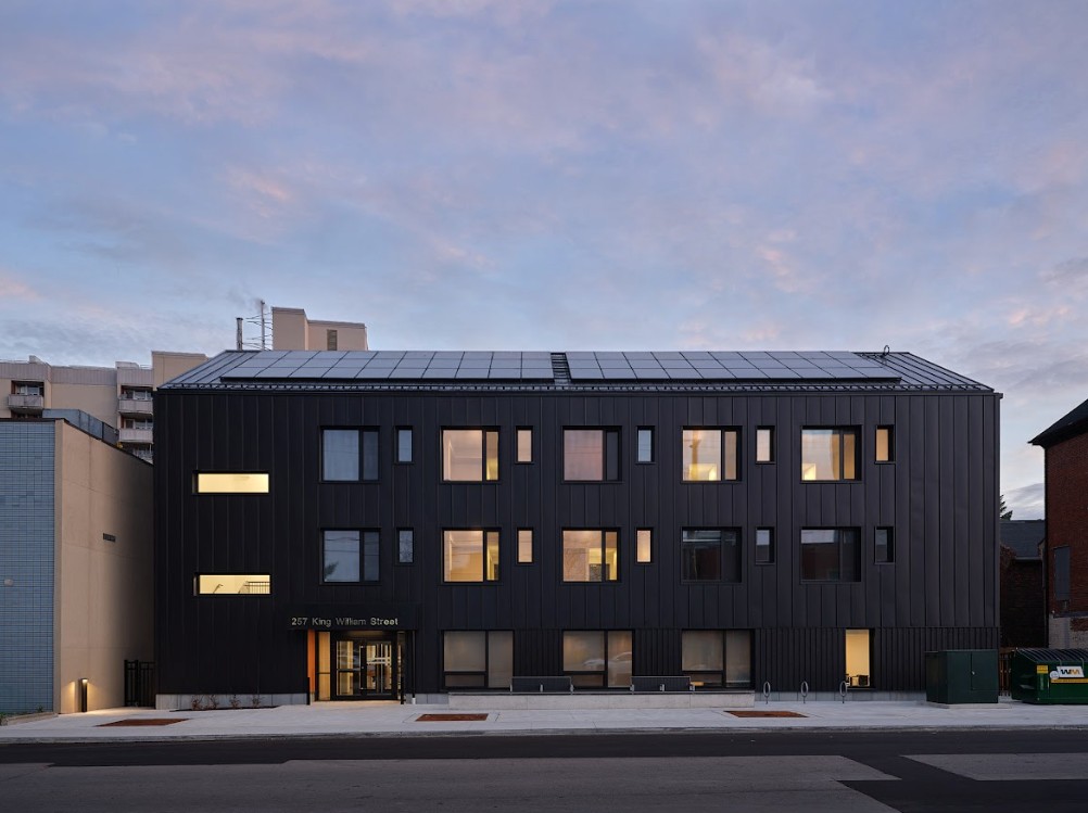 Modern black metal building at 257 King William Street with irregular windows, solar panels, and a minimalist entrance at dusk.