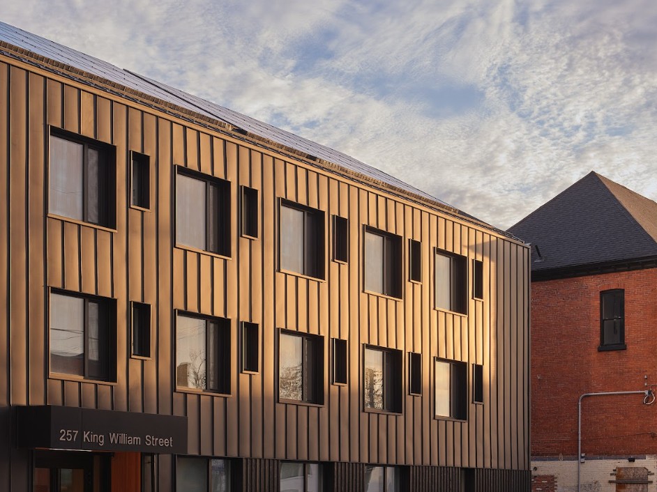 Modern building at 257 King William Street with gold-toned metal cladding, irregular windows, and solar panels, illuminated by sunlight.