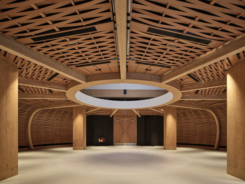 A spacious wooden interior featuring intricate lattice ceiling design, curved walls, and a subtle circular light fixture above.