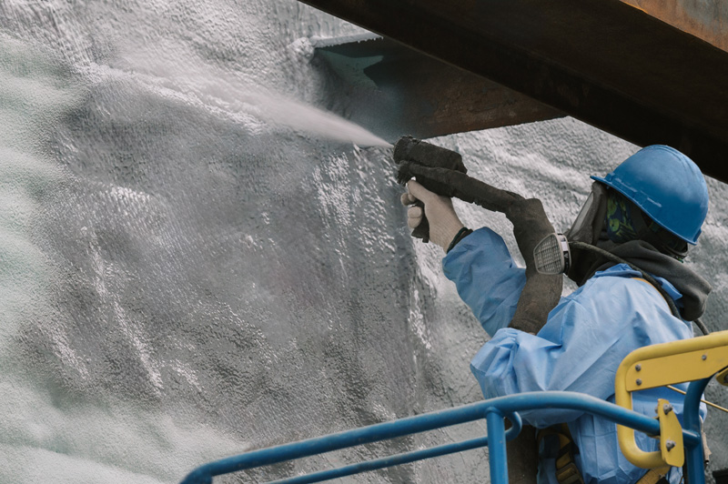 Person in protective gear applying spray foam insulation to a building structure.