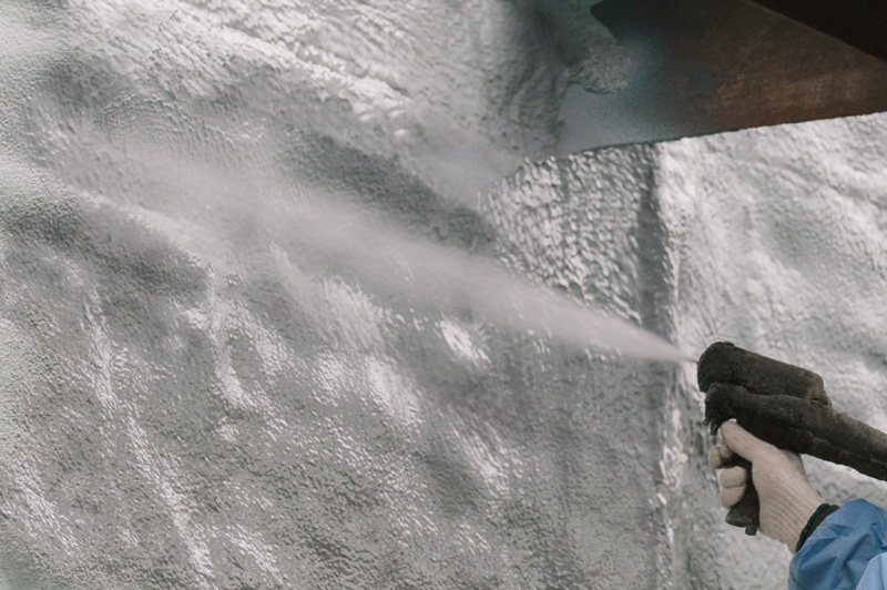 Spray foam insulation being applied to a gray exterior wall.