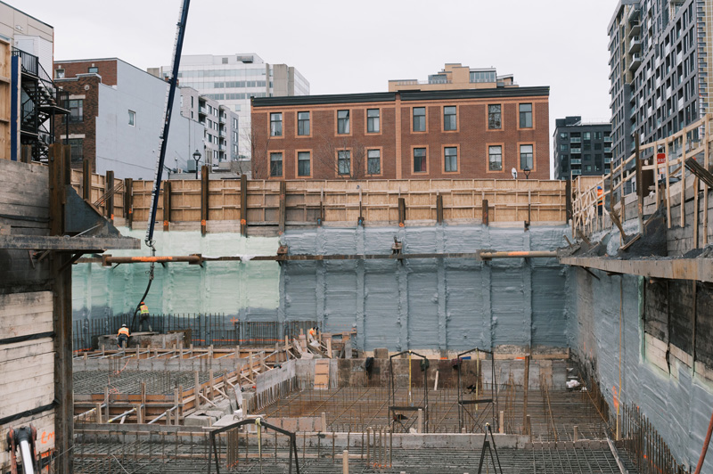 Construction site with workers, foundation, and surrounding buildings under development.