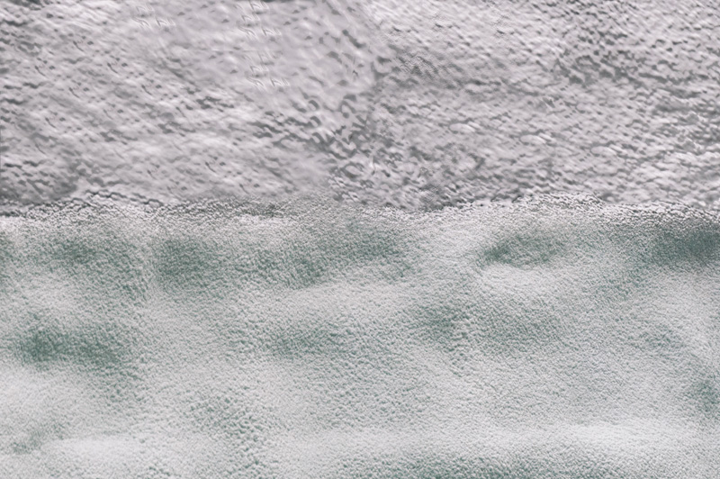 Textured gray concrete surface transitioning to a layer of light gray, foamy substance.