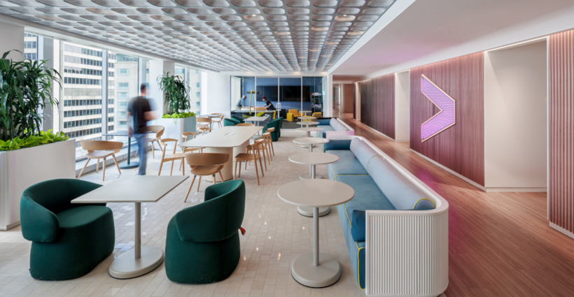 A modern office lounge with contemporary furniture, including green armchairs, white tables, and a long blue sofa.