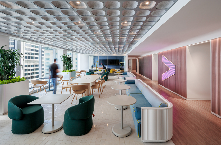 A modern office lounge with contemporary furniture, including green armchairs, white tables, and a long blue sofa.