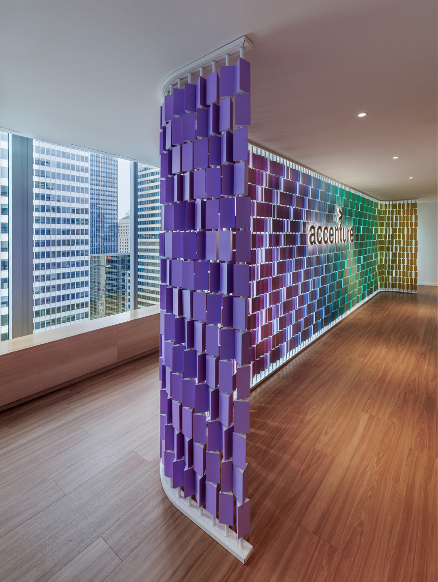 Modern office interior featuring a colorful wall display with purple and green panels, the Accenture logo, and city views outside.